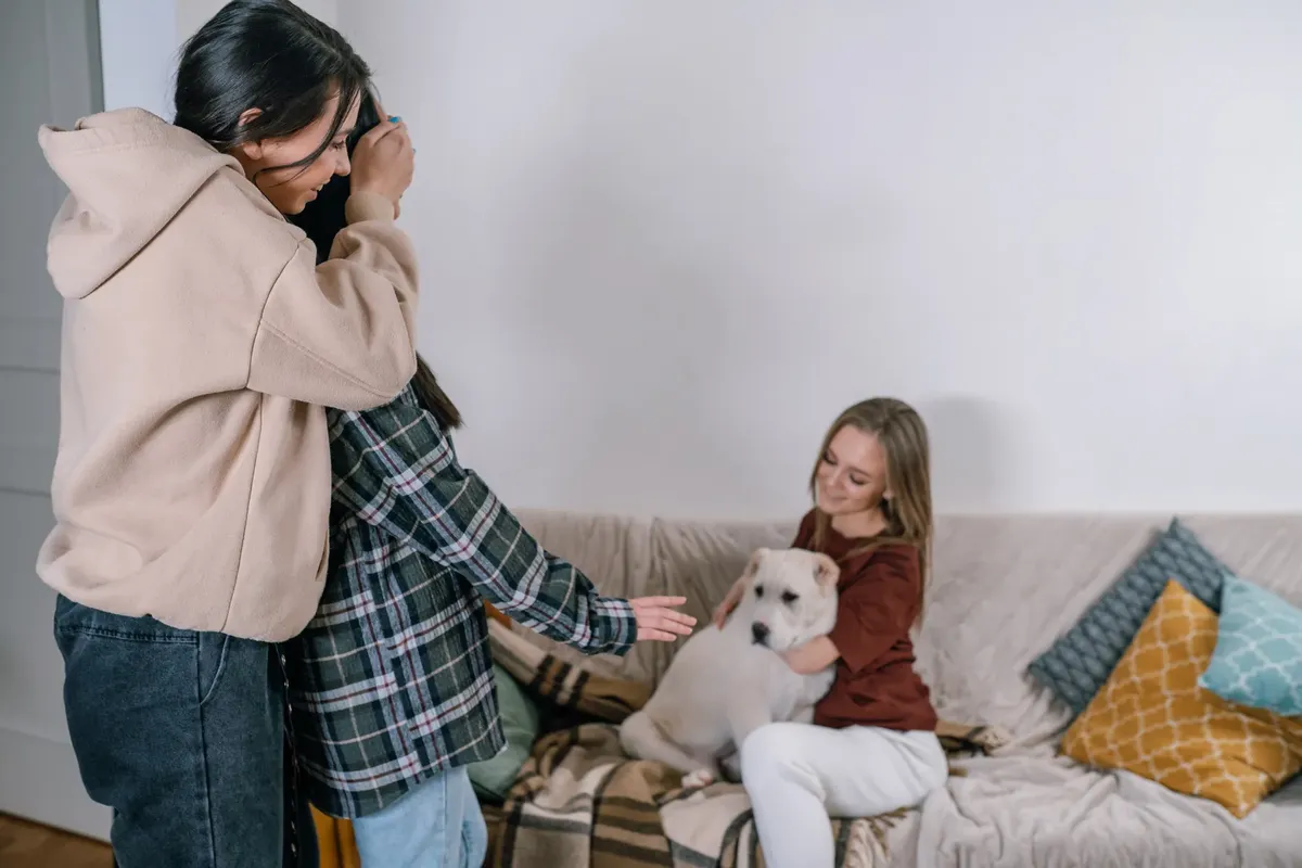 Three friends sitting on a couch with a white dog, enjoying a cozy moment together.