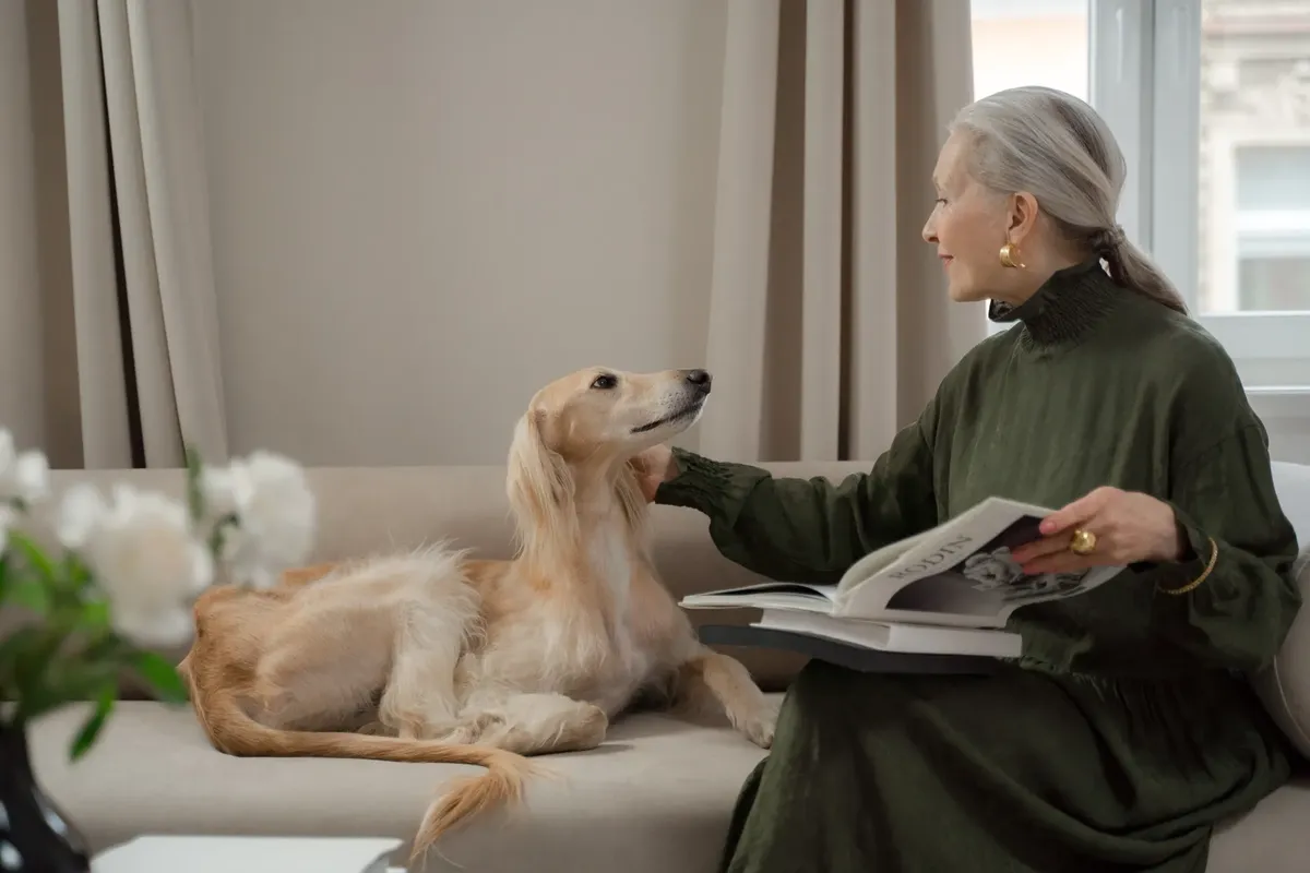 Elegant senior woman reading with a Saluki dog on a living room sofa.
